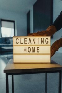 Gloved hands adjusting a lightbox sign that reads "CLEANING HOME"