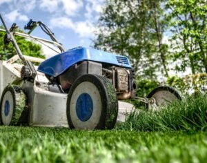 Close-up of a gas-powered lawn mower cutting grass in a garden, showing detailed wheels and blades, highlighting lawn care and outdoor maintenance.
