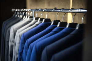 Row of blue and gray suits hanging on a metal rack in a closet, showcasing organized professional attire