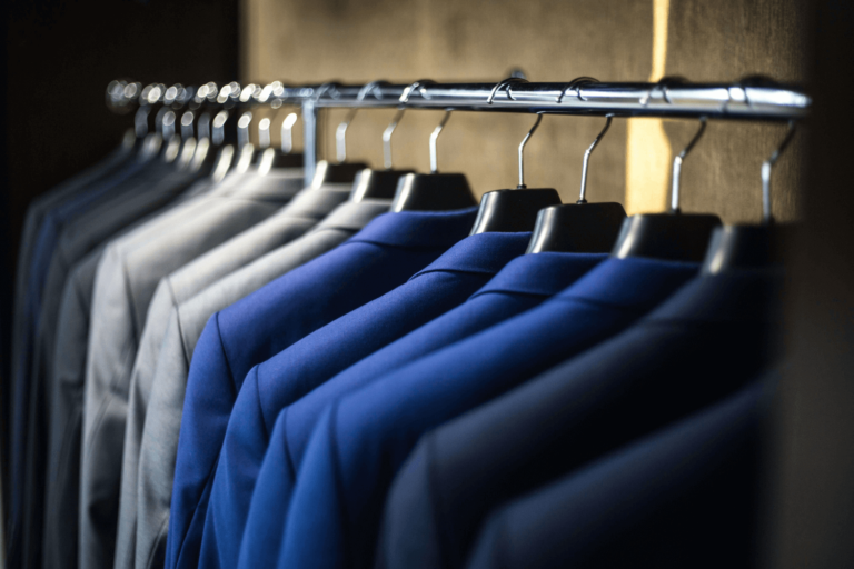 Row of blue and gray suits hanging on a metal rack in a closet, showcasing organized professional attire