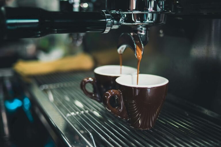 Espresso machine pouring fresh coffee into two brown ceramic cups on a metal grate