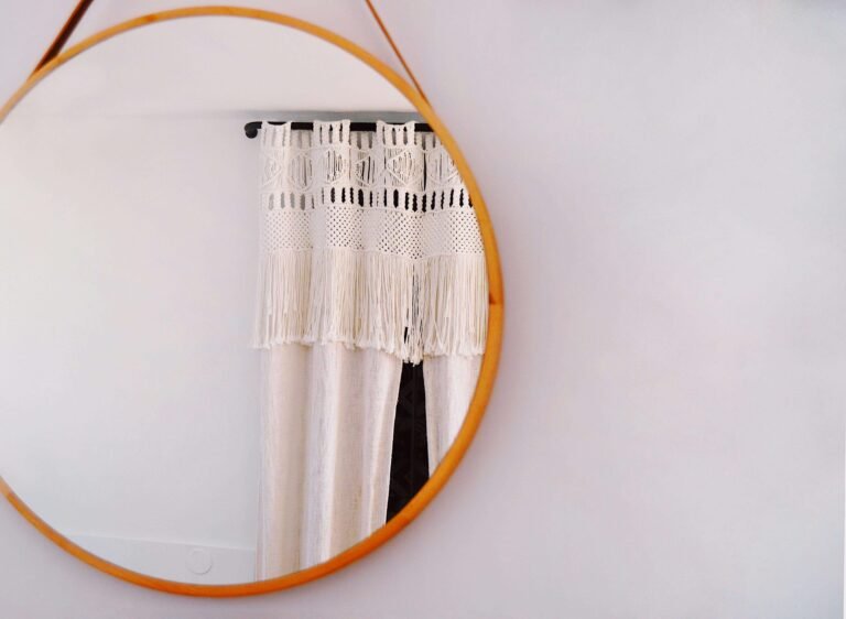 Round orange mirror reflecting a white macramé wall hanging.