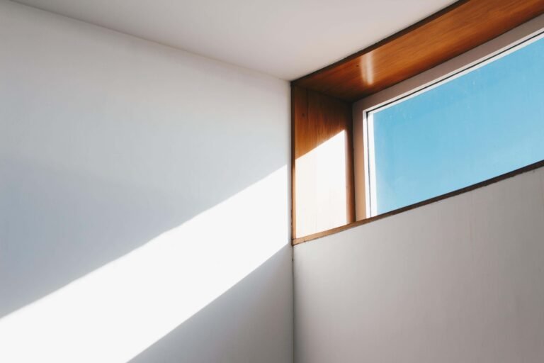 Minimalist room interior with a rectangular window, wooden frame, and sunlight casting shadows on white walls