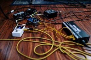 Various guitar effect pedals and audio equipment connected by yellow and black cables on a wooden floor. Close-up view of a musician's pedalboard setup, including a Mooer power supply.