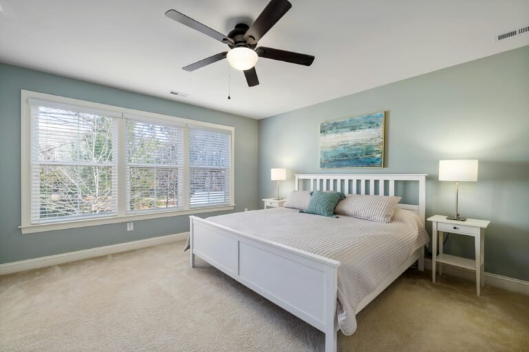 Serene bedroom with white bed, seafoam green walls, and large windows