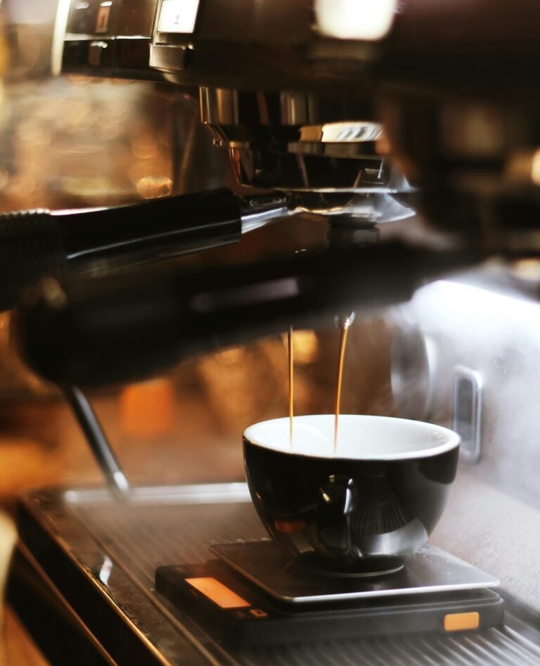 Close-up of an espresso machine brewing a fresh shot of coffee into a black ceramic cup. Two streams of rich, golden crema flow from the portafilter, with steam rising, capturing the essence of artisanal coffee-making.