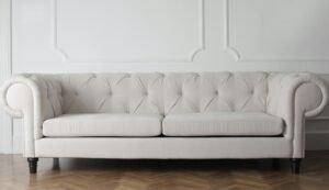 Elegant white tufted Chesterfield sofa against a white wall with decorative molding, set on a herringbone wooden floor