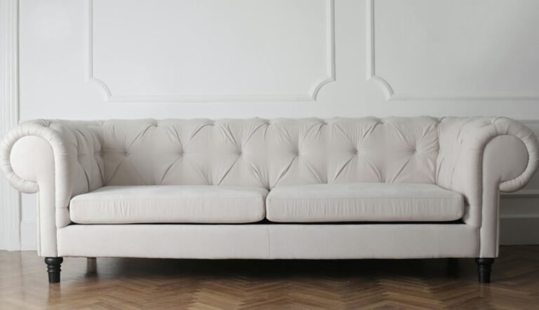 Elegant white tufted Chesterfield sofa against a white wall with decorative molding, set on a herringbone wooden floor