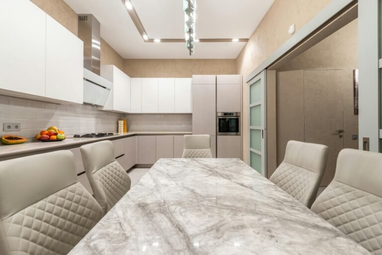 Modern white kitchen with marble countertops and quilted leather chairs