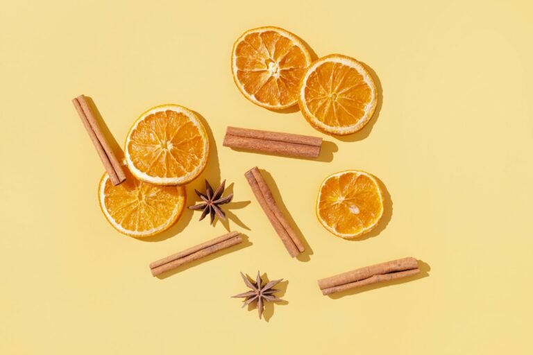 Flatlay of dried orange slices, cinnamon sticks, and star anise arranged on a pale yellow background, creating a festive and aromatic composition