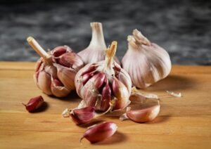 Close-up of whole garlic bulbs and individual cloves on a wooden surface, with some cloves peeled and scattered, against a dark background