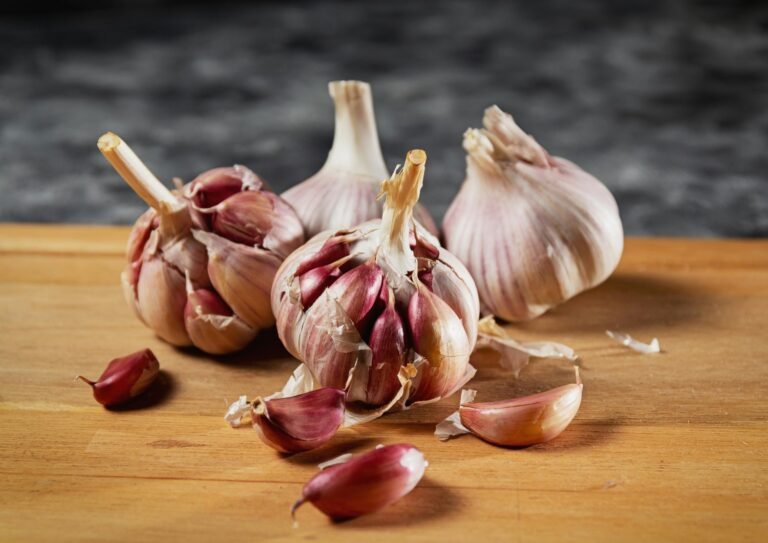 Close-up of whole garlic bulbs and individual cloves on a wooden surface, with some cloves peeled and scattered, against a dark background