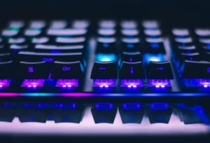 Close-up of a mechanical gaming keyboard with vibrant RGB backlighting. Keys illuminate in purple and blue hues, highlighting 'Shift' and 'Ctrl' buttons. Sleek black keycaps contrast with bright LED glow.