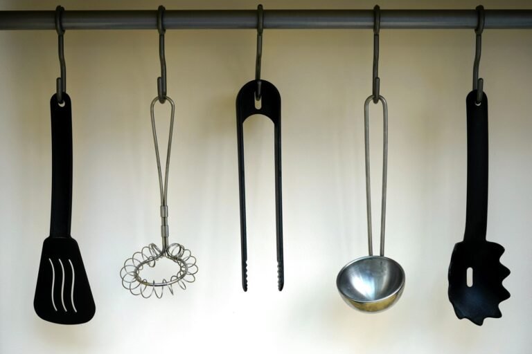 Various kitchen utensils hanging on a rack, including a spatula, whisk, tongs, ladle, and slotted spoon