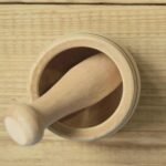 Overhead view of a wooden mortar and pestle set on a light wooden surface, highlighting the natural grain and texture of the wood