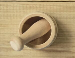 Overhead view of a wooden mortar and pestle set on a light wooden surface, highlighting the natural grain and texture of the wood