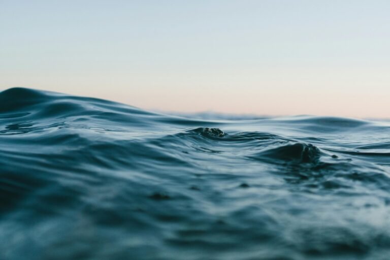 Close-up of ocean waves with gentle ripples against a pastel sunset sky