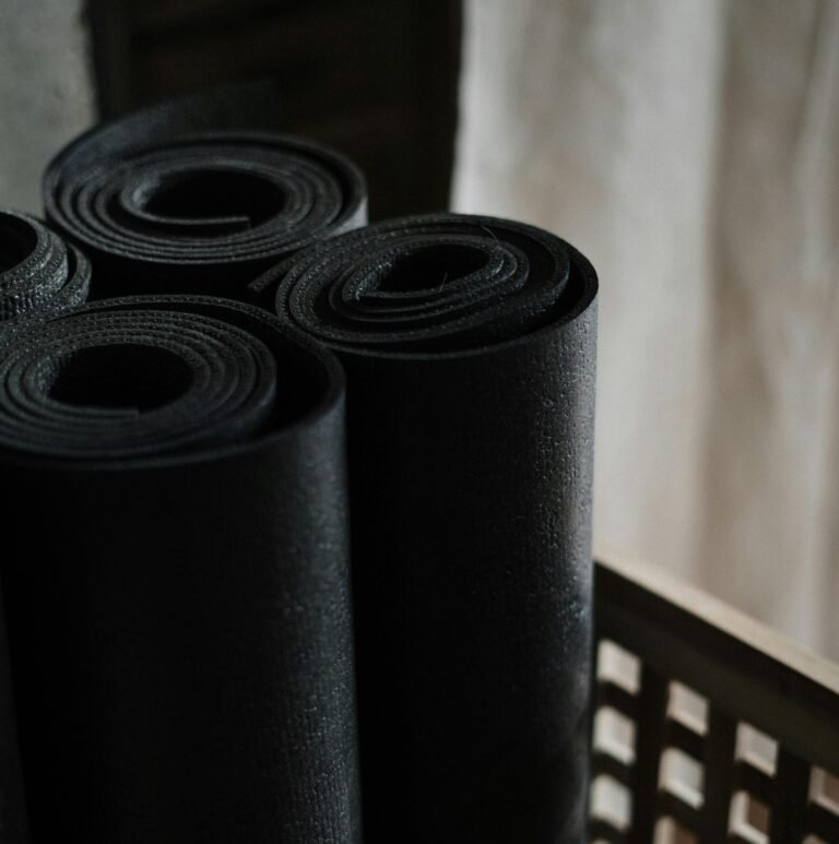 Multiple rolled-up black yoga mats stacked vertically, showcasing their dense foam texture and cylindrical shape against a light background.