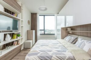 Modern bed with built-in shelving in a bright bedroom overlooking the city, featuring sleek neutral accents.