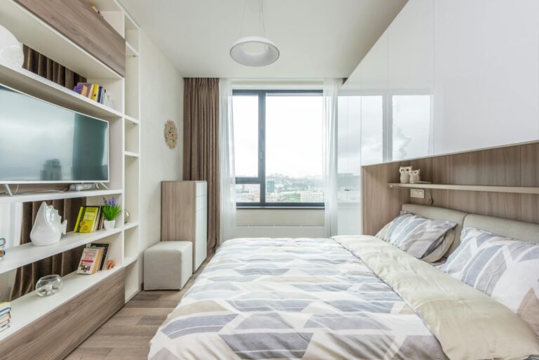 Modern bed with built-in shelving in a bright bedroom overlooking the city, featuring sleek neutral accents.