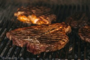 Thick steaks sizzling on an outdoor grill.