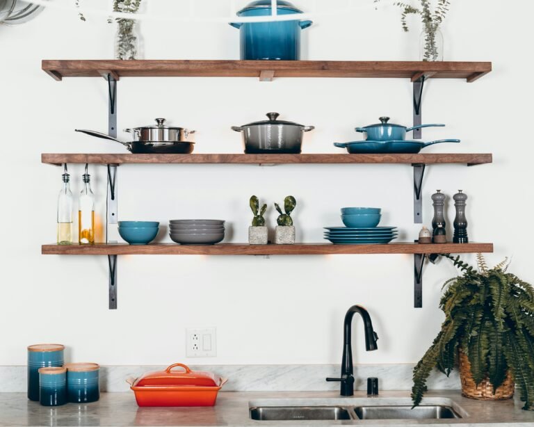 Kitchen shelves with vibrant pots and dinnerware against a light wall.