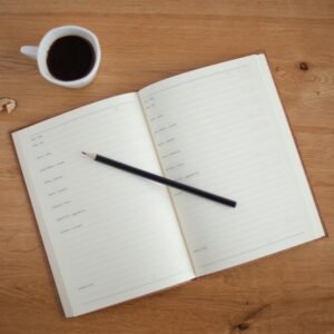 Wooden table with an open notebook, pen, and cup of coffee