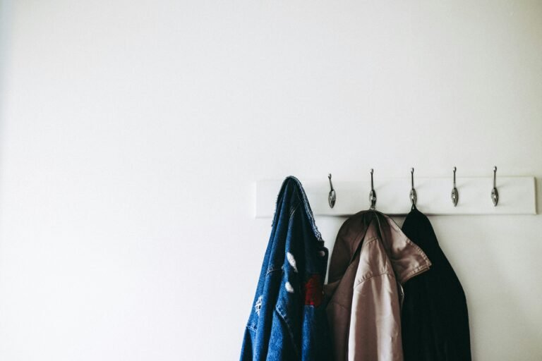 Row of jackets hanging on wall hooks in a white entryway
