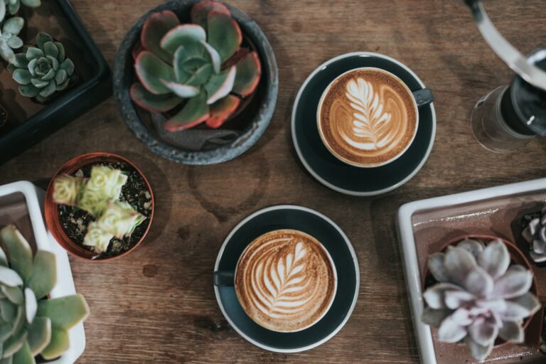 Cup of latte art on a wooden tray surrounded by succulents