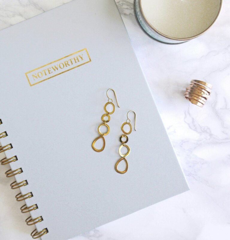 Open planner notebook with gold disc-binding, next to small accessories on a marble desk.