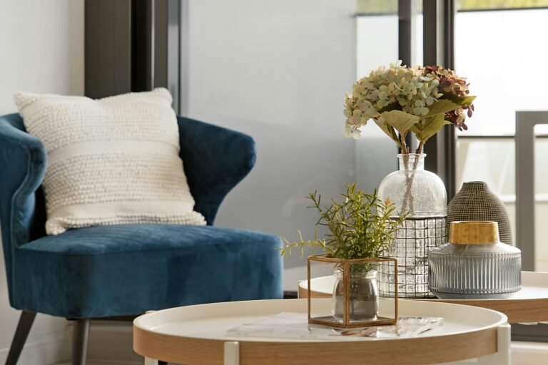 Comfortable blue armchair next to a table with a vase of flowers.