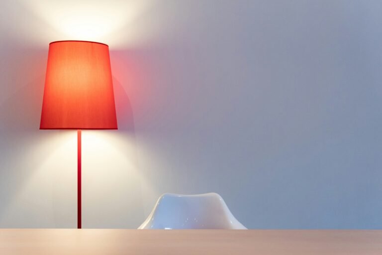 Softly lit red lamp on a simple table against a pale wall.