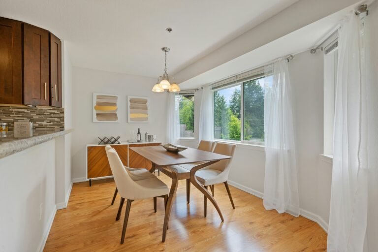 Sunlit dining space featuring a round wooden table and minimalist chairs.