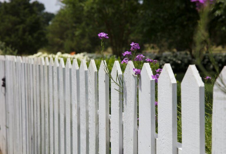 Classic white picket fence with greenery in the background.