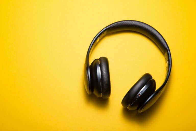 Black wireless headphones placed on a bright yellow surface.