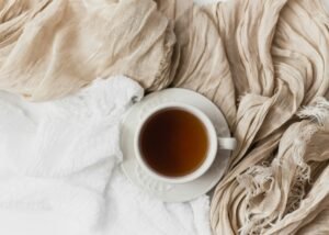 Cup of hot beverage placed on soft, neutral-toned textiles.