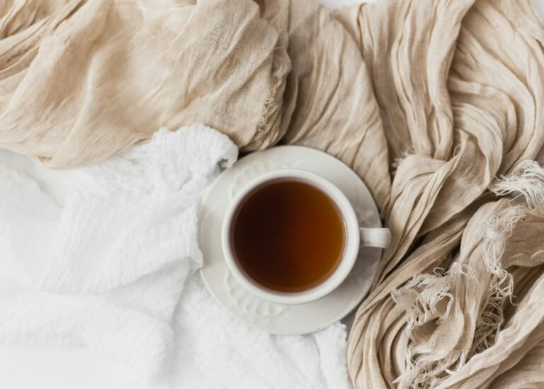 Cup of hot beverage placed on soft, neutral-toned textiles.