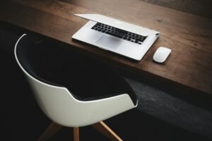Minimalist home office setup with a laptop and white chair on a wooden desk.
