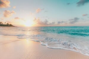Tranquil beach scene at sunrise with pastel sky and calm ocean.