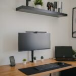 Clean wooden desk with a single monitor and potted plant